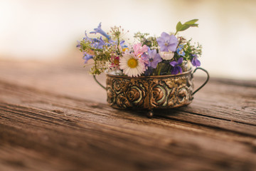 Lovely bouquet of meadow flowers in a small vase on a rustic wooden background. Shallow depth of field, soft effect.