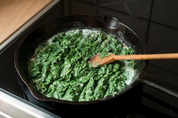 Preparation of a dish - baby spinach boiled in garlic sauce in a cast-iron pan.