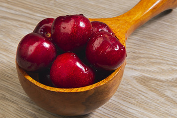 Beautiful photograph of a handful of cherries in a wooden spoon