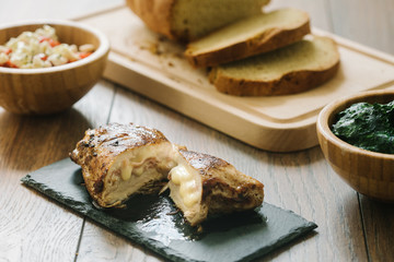 Grilled, stuffed chicken breast on a stone plate with homemade bread, salad and spinach as side dish.