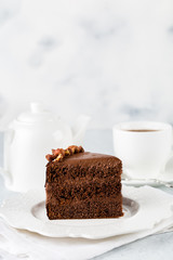 A piece of chocolate cake with nuts on light background and cup of tea. Copy space