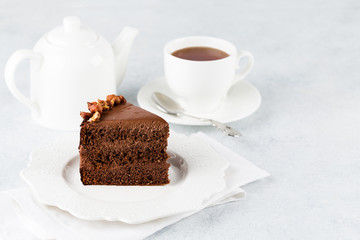 A piece of chocolate cake with nuts on light background and cup of tea. Copy space