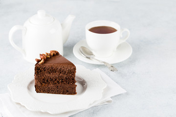 A piece of chocolate cake with nuts on light background and cup of tea. Copy space