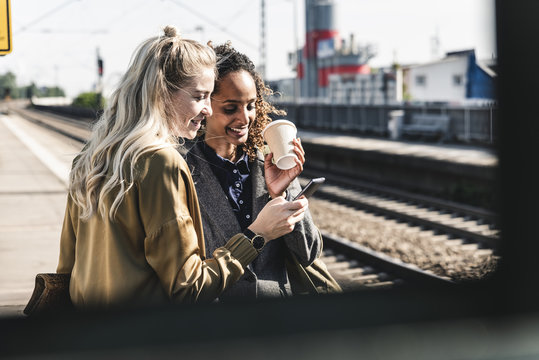 Friends waiting at train station looking at smartphone