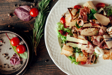 meat salad with bacon, cheese, vegetables and croutons at dark wood table