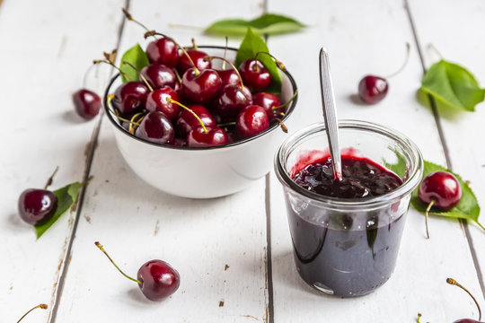 Jar of cherry jam and cherries on white wood