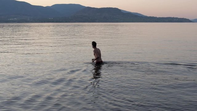 Slow Motion Man Wading Into Lake and Diving Underwater at Sunset