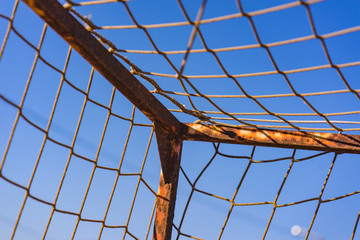 Old vacant football soccer goal gate on front of the blue ocean. Old sports field with rusty goal and net on meadow with muddy front line.