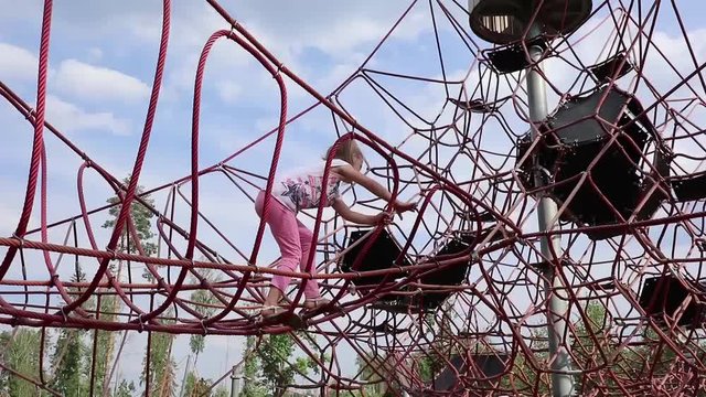young girl climbs on the Playground on the grid