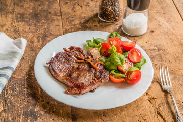 Delicious fried steak with fresh salad of spinach and cherry tomatoes in a white plate on a rustic table