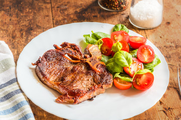 Delicious fried steak with fresh salad of spinach and cherry tomatoes in a white plate on a rustic table