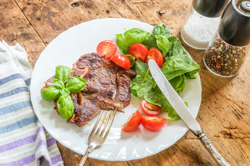 Delicious fried steak with fresh salad of spinach and cherry tomatoes in a white plate on a rustic table