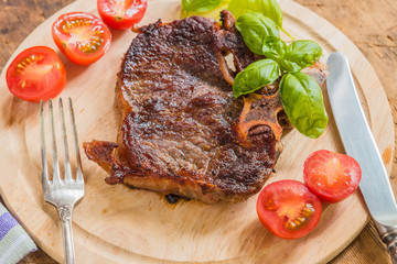 Delicious roast steak with fresh cherry tomatoes and basil leaves on a wooden plate