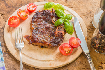 Delicious roast steak with fresh cherry tomatoes and basil leaves on a wooden plate