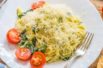 Delicious vegetarian pasta with spinach cream sauce on a white plate with cherry tomatoes