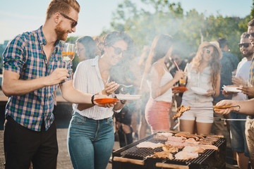 Group of people standing around grill, chatting, drinking and eating.  - obrazy, fototapety, plakaty