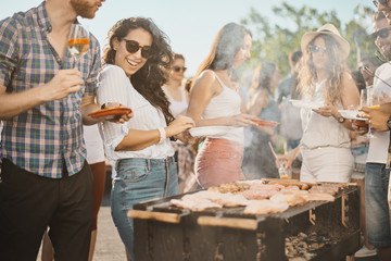 Fototapeta na wymiar Group of people standing around grill, chatting, drinking and eating. 