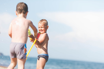 A little boy has fun playing with his water gun on the sea 