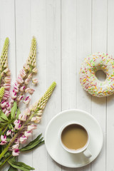 Still life with a Cup of coffee and lupine flowers donut on a light wooden table