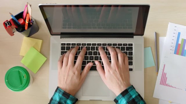 Office worker typing text on laptop and drinking coffee from a paper cup