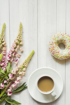 Fototapeta Still life with a Cup of coffee and lupine flowers donut on a light wooden table