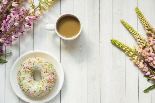Fototapeta Still life with a Cup of coffee and lupine flowers donut on a light wooden table