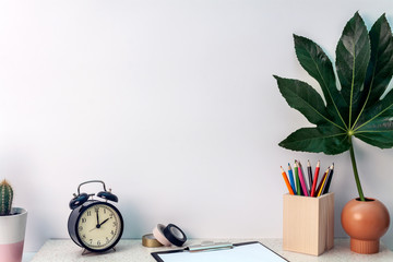 Desk with a patterned table top with a clock, cactus, crayons and a leaf in a vase