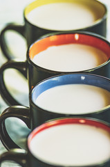 Black mugs with milk stand in a row