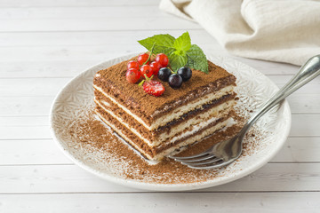 Delicious Tiramisu cake with fresh berries and mint on a plate on a light background.