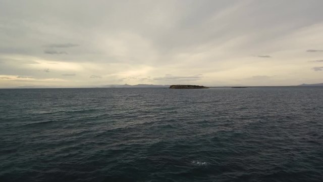 Flying over the sea on a cloudy day. Small island on the horizon.