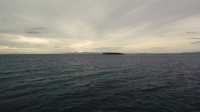 Flying over the sea on a cloudy day. Small island on the horizon.