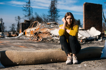 Sad woman home owner holds his head by hand checking burnt out house and yard after fire disaster,...