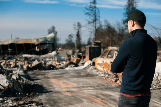 Man owner checking burned and ruined house and yard after fire, consequences of fire disaster accident. Ruins after fire disaster.