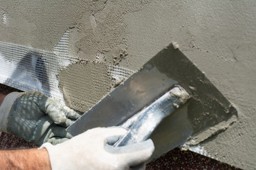 Closeup hand construction plastering wet cement on expanded polystyrene