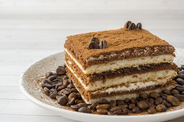 Delicious Tiramisu cake with coffee beans on a plate on a light background