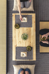 Real photo of three people sitting around wooden table drinking a tea in japanese living room interior
