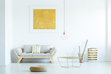 Pouf and table near grey sofa under yellow painting in modern living room interior. Real photo