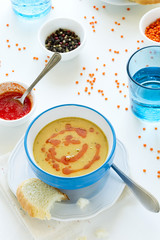 Red lentil soup with chili pepper sauce and bread on white wooden table