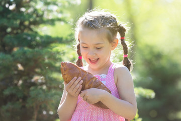 A child bites bread in nature. A little girl is eating a sweet bun in a city park.