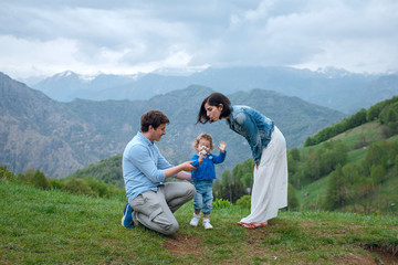 Young family of parents and their daughter spending time in mountains. Mother blowing on dandelions.