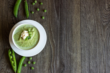 Green peas soup with spinach and cream on rustic background.