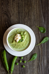 Green peas soup with spinach and cream on rustic background.