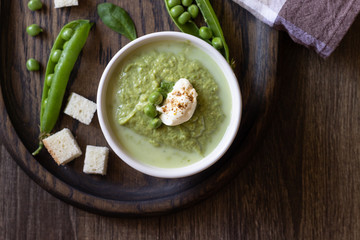 Green pea soup in bowls with spinach and cream on wooden rustic cutting board.