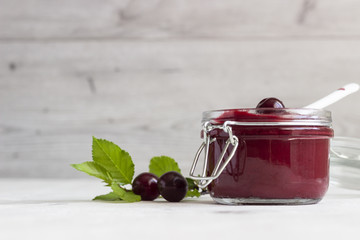 Homemade cherry jam in a jars with fresh cherries on a light background.