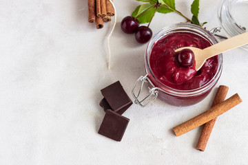 Homemade cherry jam with chocolate, spices (cinnamon, nutmeg) with fresh cherries in a jar on a...