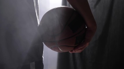 Close footage of basketball player holding ball, standing in dark misty room