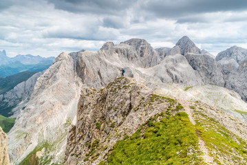 Fototapeta na wymiar Panoramic view of a climber standing on the top of cliff in Dolomites Mountains. Italian Dolomites. Panoramic view of man walking on the ridge of the rocky mountains. 
