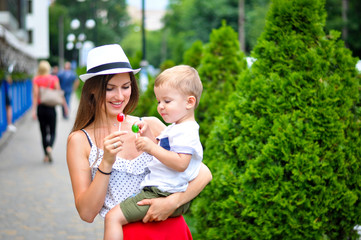 A young mother in a white hat is holding a two-year-old son and eating colored candies