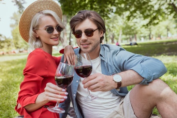 happy couple clinking with glasses of wine in park