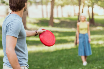 young couple playing frisbee with red frisbee disk in park - obrazy, fototapety, plakaty